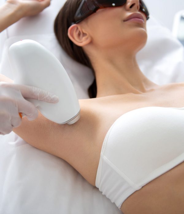 Aesthetic body treatment. Close up portrait of young relaxed beautiful woman in white underwear lying on couch and having laser hair removal procedure of armpit